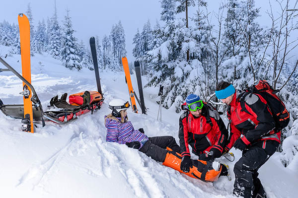 A skiier laying in snow being assisted by medical personnel A skiier laying in snow being assisted by medical personnel