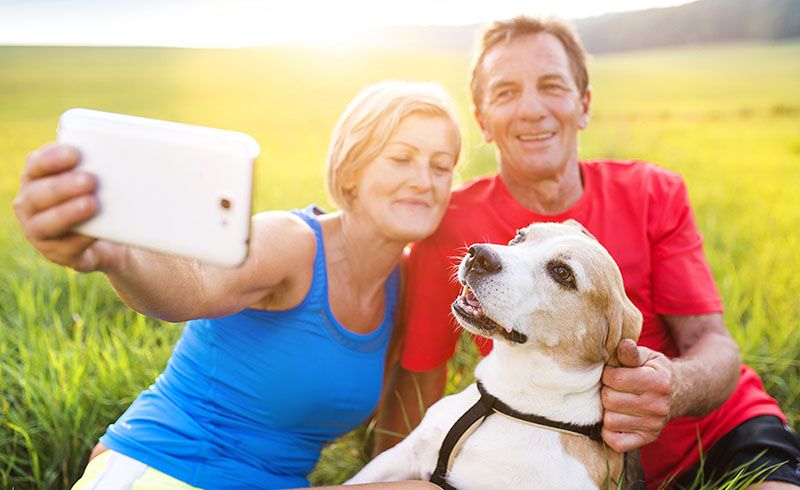 A woman, man, and a dog sat on a field taking a selfie
